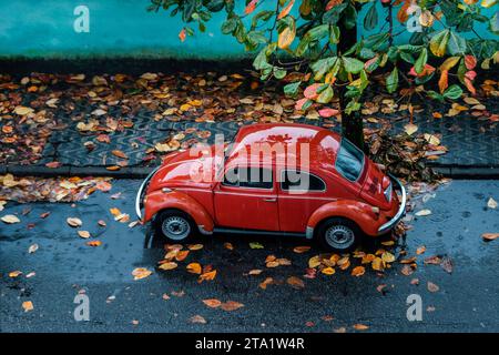 Der alte rote Volkswagen Käfer parkte an einem regnerischen Herbsttag auf der Straße. Stockfoto