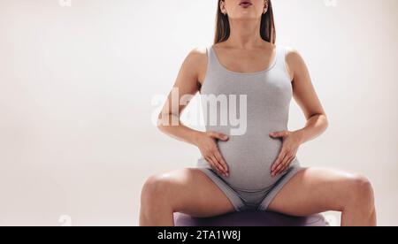 Schwangere Frau im dritten Trimenon übt pränatalen Yoga in einem Studio. Mit einem Stabilitätsball für Halt konzentriert sie sich auf Flexibilität und Stärke Stockfoto