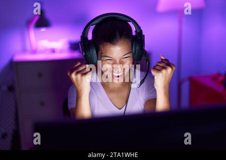 Junge schöne hispanische Frau streamer spielen Videospiel mit Sieger Ausdruck in Gaming-Raum Stockfoto