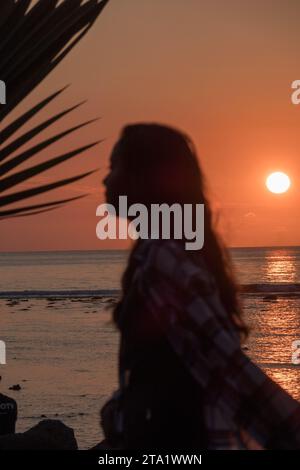 Ein junges Mädchen in Silhouette bei Sonnenuntergang über dem Indischen Ozean, St-Leu, Reunion Island, Frankreich. Stockfoto