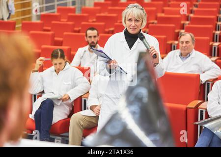 Ärztin im Publikum der medizinischen Konferenz, die beim Halten des Dokuments im Auditorium eine Frage an den Sprecher stellt Stockfoto