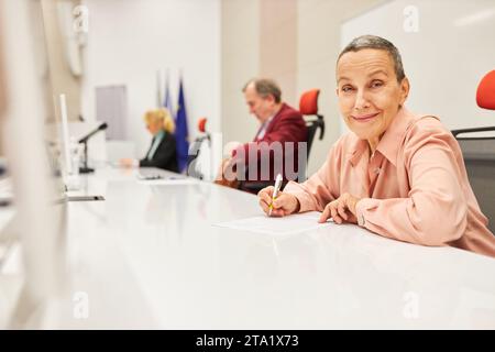 Porträt einer lächelnden Sprecherin, die im Dokument schreibt, während sie an der Tafel im Kongresszentrum sitzt Stockfoto