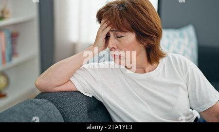 Eine Frau mittleren Alters, gestresst auf dem Sofa zu Hause zu sitzen Stockfoto