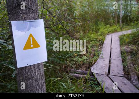 Gelbes Dreieck-Warnschild neben hölzernen Entenbrettern im Wald Stockfoto