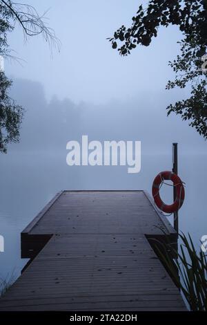 Hölzerner Pier im blauen Morgennebel, mit einem Rettungsring, der an einer Stange hängt Stockfoto