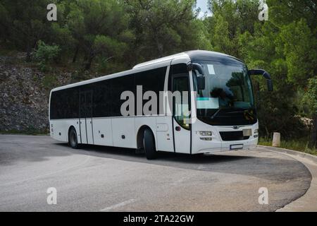 Weißer Touristenbus, der durch eine enge Haarnadelkurve auf einer Bergstraße fährt Stockfoto