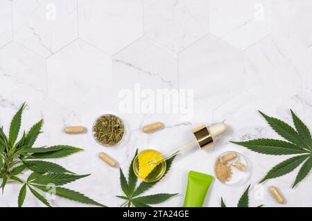 Kosmetik, CBD-Öl, Hanfpulverkapseln, trockener Tee und grüne Cannabis-Sativa-Blätter auf einem Marmortisch, Mockup, Kopierraum. Biologische Hautpflege BE Stockfoto