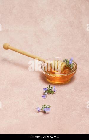 Natürlicher Honig in einer Glasschale mit einem Holzlöffel und frischen Rosmarinzweigen in Blüte Stockfoto