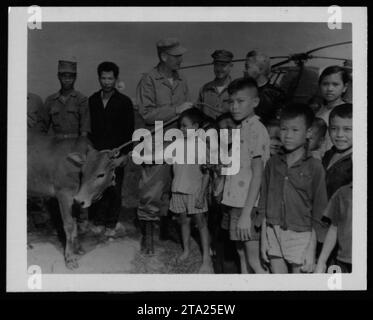 US-amerikanischer Soldat, der während des Vietnamkrieges 1962 einen vietnamesischen Zivilisten medizinisch versorgt. Der Soldat wird gesehen, wie er den Arm eines Jungen bandagiert, während eine Gruppe von Dorfbewohnern zusieht. Dies spiegelt die Interaktion von Mensch zu Mensch wider, in der amerikanische Truppen mit Zivilisten zusammenarbeiteten und humanitäre Hilfe leisteten. Stockfoto