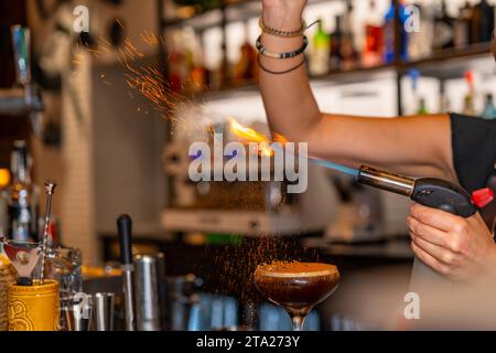 Nahaufnahme der Hände eines Barkepers, der in einer Bar mit einer Taschenlampe die Toppings eines Kaffeekoztails verbrennt Stockfoto