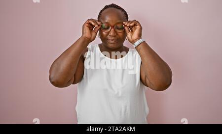 Cool und entspannt, eine übergewichtige afroamerikanische Erwachsene Frau steht bereit, ihr ernster Ausdruck versteckt sich hinter einer Brille. Sie ist isoliert über einem rosa W Stockfoto