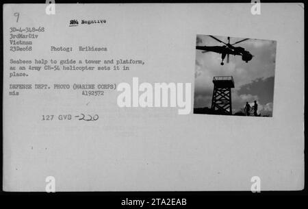 Seabees helfen dabei, einen Turm und eine Plattform in Position zu bringen, während ein Army CH-54 Hubschrauber ihn absenkt. Dieses Foto, das am 23. Dezember 1968 während des Vietnamkriegs aufgenommen wurde, zeigt militärische Aktivitäten mit Hubschraubern. Es ist ein Negativfoto, das von der Fotog Bribiesca aufgenommen wurde und zur Marine Corps-Sammlung des Verteidigungsministeriums gehört. Die Bildreferenznummer ist A192572-127, die der 3. Marine Division in Vietnam zugeordnet ist. Stockfoto