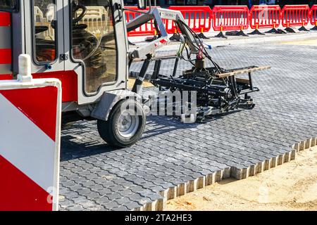 Pflasterblock-Verlegemaschine auf neuem Pflaster, rote Kunststoffbarrieren, Warnschild, neu gestalteter Platz Stockfoto