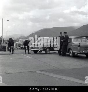 1950er Jahre, historisch, ein Autounfall am Eingang zu einem Stahlwerk, an dem zwei Autos dieser Zeit beteiligt waren, ein Wolsley 1500 und Austin Cambridge mit Anwesenheit der Polizei. Gesehen wird das Polizeifahrzeug, ein Ford Zephyr Zodiac, ein großer Personenwagen, der 1955 eingeführt wurde. Das Auto hat keine Markierungen, nur das Wort Polizei in der Heckscheibe. Einer der Polizisten hat ein Maßband Stockfoto