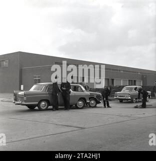 1950er Jahre, historisch, ein Autounfall am Eingang zu einem Stahlwerk, an dem zwei Autos dieser Zeit beteiligt waren, ein Wolsley 1500 und Austin Cambridge mit Anwesenheit der Polizei. Gesehen wird das Polizeifahrzeug, ein Ford Zephyr Zodiac, ein großer Personenwagen, der 1955 eingeführt wurde. Das Auto hat keine Markierungen, nur das Wort Polizei in der Heckscheibe. Einer der Polizisten hat ein Maßband Stockfoto