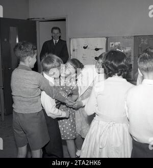 1960er Jahre, historische Grundschule, in einem Klassenzimmer, aufgeregt Jungs und Mädchen spielen ein Partyspiel... Augen geschlossen für einen Kuss! Fife, Schottland, Großbritannien Stockfoto