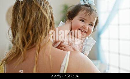 Glückliche Mutter steht zuversichtlich zu Hause, hält ihre liebenswerte Tochter in den Armen und genießt gemeinsam die Liebe der Familie in ihrem Wohnzimmer mit einem Stockfoto