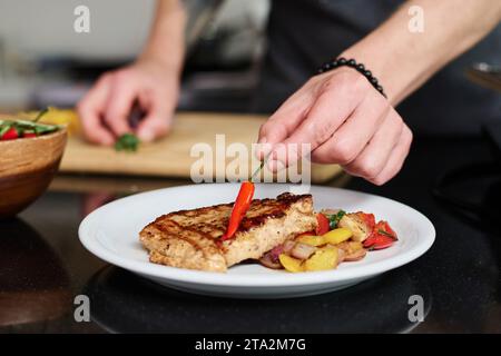 Nahaufnahme der Hand eines nicht erkennbaren Mannes, der Chili auf frisch gekochtes Stück Fleisch legt, mit Gemüse herum, Kopierraum Stockfoto