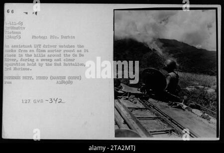 Während einer Kehrfahrt in Vietnam blickt ein Assistenzfahrer auf dem Landing Vehicle Raupenfahrzeug (LVT) zu, während der Rauch aus einem 81-mm-Mörserumlauf in den Hügeln um den CA de River steigt. Das Foto wurde am 13. August 1965 von PFC Durbin von der 3. Marine Division aufgenommen. Stockfoto