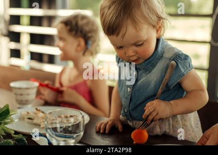 Porträt eines kleinen Mädchens, das mit einer Gabel eine Aprikose vom Küchentisch nimmt. Stockfoto