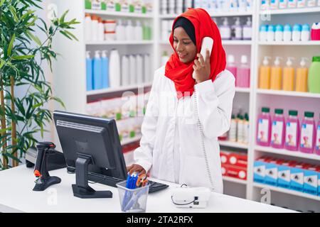 Eine junge, schöne Apothekerin, die telefoniert, indem sie einen Computer in der Apotheke benutzt Stockfoto