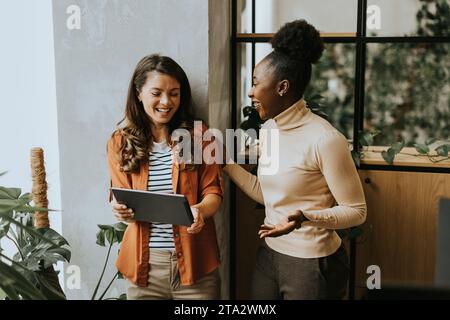 Zwei hübsche junge Geschäftsfrauen mit digitalem Tablet stehen im modernen Büro Stockfoto