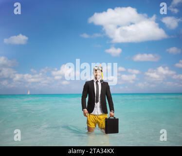 Geschäftsmann im Badeanzug mit Schnorchelflossen und Maske, der eine Aktentasche hält und im Meer steht Stockfoto