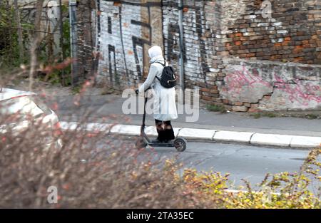 Belgrad, Serbien - 2. Dezember 2020: Eine Frau, die im Winter von hinten auf einer Vorstadtstraße mit einem Elektroroller fährt Stockfoto