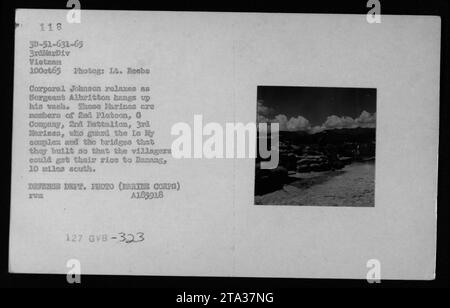 Marinekorporal Johnson entspannt sich, während Sergeant Albritton seine Wäsche auflegt. Beide sind Mitglieder des 2. Platoon, der G-Kompanie, des 2. Bataillons, der 3. Marines. Ihre Mission ist es, den Le My Komplex und die Brücken zu bewachen, die sie gebaut haben, um den Transport von Reis aus dem benachbarten Dorf Danang zu gewährleisten, das sich 10 Meilen südlich befindet. Das Foto wurde am 10. Oktober 1965 während des Vietnamkrieges aufgenommen. Stockfoto