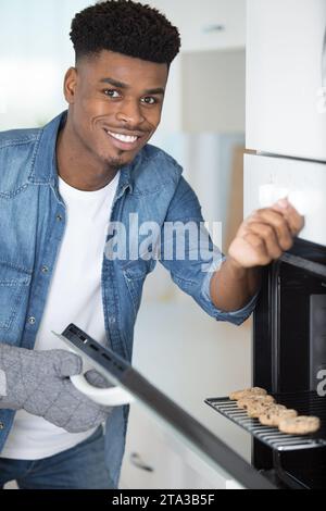 Ein hübscher Mann, der ein Tablett mit gebackenen Plätzchen aus dem Ofen herausnahm Stockfoto