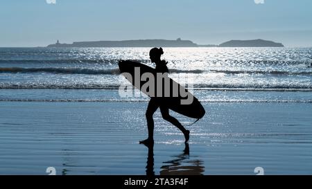 Silhouette eines unbekannten Mannes mit Surfbrett, der am Strand von Essaouira, Marokko, spaziert, der eine perfekte Mischung aus Wind und Wellen bietet Stockfoto