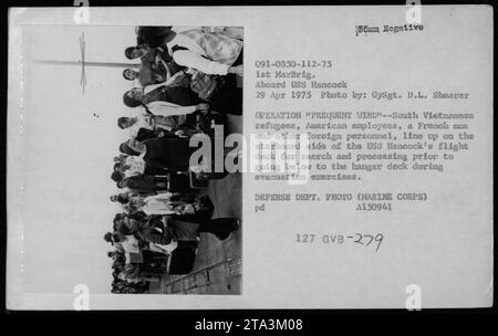 Südvietnamesische Flüchtlinge, amerikanische Mitarbeiter, eine französische Nonne und ausländisches Personal stehen am 29. April 1975 auf dem Flugdeck der USS Hancock zur Suche und Bearbeitung an, um die Operation Frequent Wind Evakuation Exercises durchzuführen. Stockfoto
