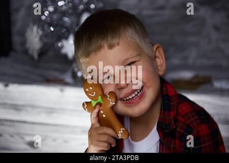 Entzückende fröhliche Kind versteckt sich hinter Weihnachten Lebkuchen und macht einen lustigen Gesichtsausdruck. Stimmungsvolles, ästhetisches Zuhause für Silvester. Fröhlich Stockfoto