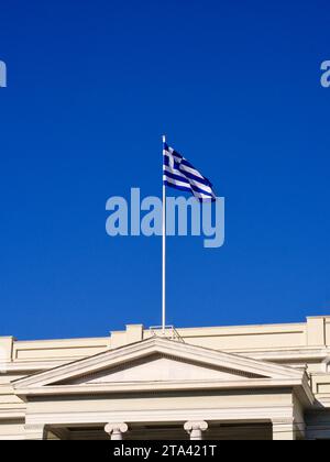 Griechische Flagge auf dem Pfosten über dem Dach des klassischen Gebäudes Stockfoto