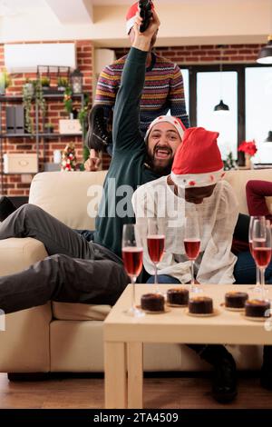 Glücklicher Mitarbeiter mit Joystick gewinnt Videospiel, während er weihnachten mit Kollegen im Büro feiert. Begeisterter Mitarbeiter, der ein Gamepad hält, während er eine Neujahrsparty genießt Stockfoto