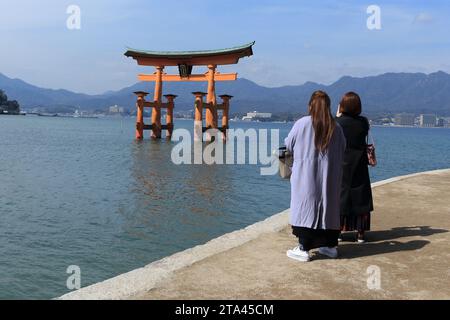 Japan Vermilion Torii Itsukushima-Jinja auf Miyajima. Zwei Frauen, die die Torii in Ruhe betrachten. Spirituell entspannend, friedlich, romantisch und friedlich. Stockfoto