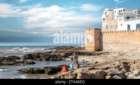 Essaouira, Marokko - 17. September 2022: Marokkanische Familie, die sich am Meer in der Nähe der Stadtmauerbastion Essaouira und der Zitadelle des Stadthafens Essaouira entspannt Stockfoto