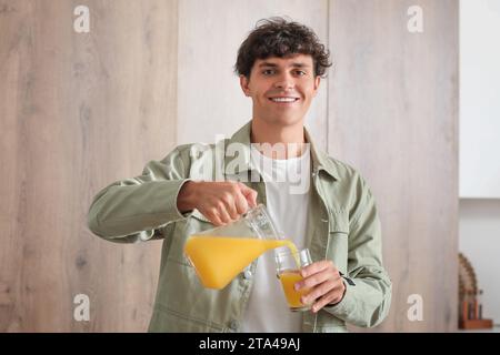 Junger Mann, der Orangensaft in die Küche gießt Stockfoto