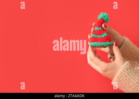 Weibliche Hände mit roter Maniküre, die gestricktes Weihnachtsbaumspielzeug auf farbigem Hintergrund halten Stockfoto