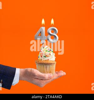 Hand hält Geburtstagskuchen mit Zahl 48 Kerze - Hintergrund orange Stockfoto