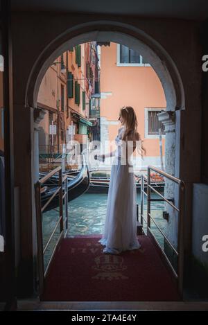 Elegante Braut in atemberaubendem weißem Hochzeitskleid posiert im traditionellen venezianischen Bogengang Stockfoto