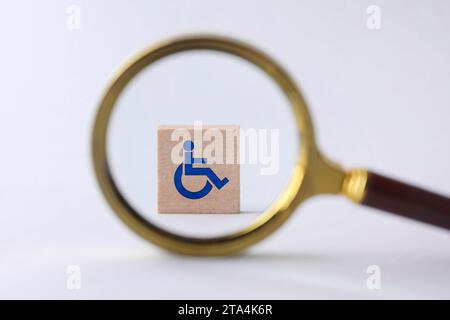 Inklusionskonzept. Holzwürfel mit internationalem Zugangssymbol, Blick durch Lupe Stockfoto