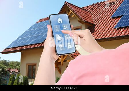 Frau mit Smart Home Control System per Handy in der Nähe von Haus draußen, Nahaufnahme Stockfoto