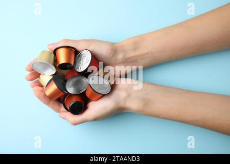 Frau, die einen Haufen Kaffeekapseln auf hellblauem Hintergrund hält, Ansicht von oben Stockfoto