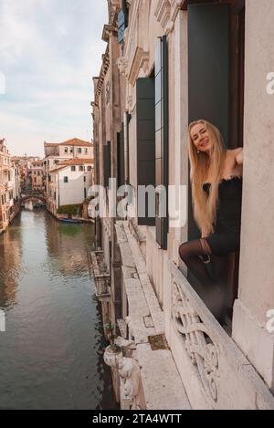 Elegante Frau in schwarzem Kleid, die die klassische venezianische Architektur und den Blick auf den Kanal bei Tageslicht genießt Stockfoto