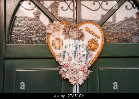 Wunderschöner herzförmiger Kranz, der an der grünen Tür hängt, mit unbekannter Umgebung und Details Stockfoto