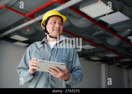 Lächelnder vietnamesischer Bauarbeiter mit Tablet-Computer, der die Baustelle inspiziert Stockfoto