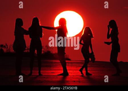 Isle Of Palms, Usa. Juli 2023. Junge Frauen bilden mit ihren Händen ein Herz, während sie sich vor einem dramatischen Sonnenaufgang als riesiger Ball über dem Strand in Isle of Palms, South Carolina, am Sonntag, den 9. Juli 2023, in Silhouetten verwandeln. Wie viele Teile des Landes erlebt auch das Charleston Low Country extrem heißes, feuchtes Wetter. Foto: Richard Ellis/UPI Credit: UPI/Alamy Live News Stockfoto