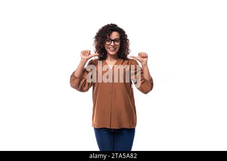 Junge, gepflegte weiße Frau mit lockigen schwarzen Haaren steht nachdenklich auf weißem Hintergrund mit Kopierraum Stockfoto
