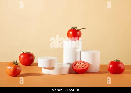 Frische Tomaten und weiße Podeste auf orange-beigem Hintergrund. Viel Platz für die Produktpräsentation, die das Konzept der veganen Kosmetik verkörpert. Stockfoto